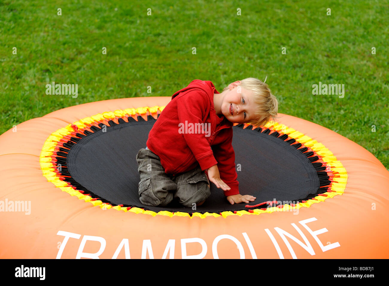 Blond Child Boy Jumping on orange Trampoline in Yard Stock Photo