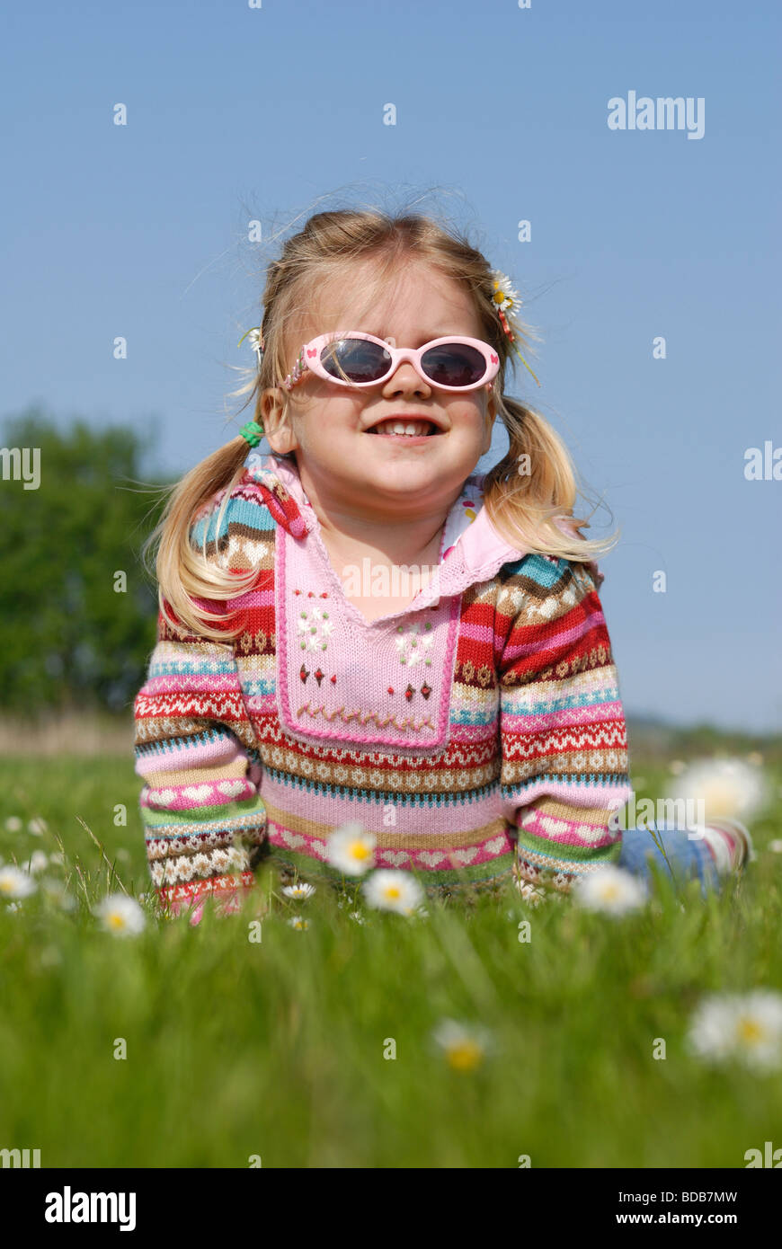 A little girl with flowers in her hair lying in the grass on a sunny ...