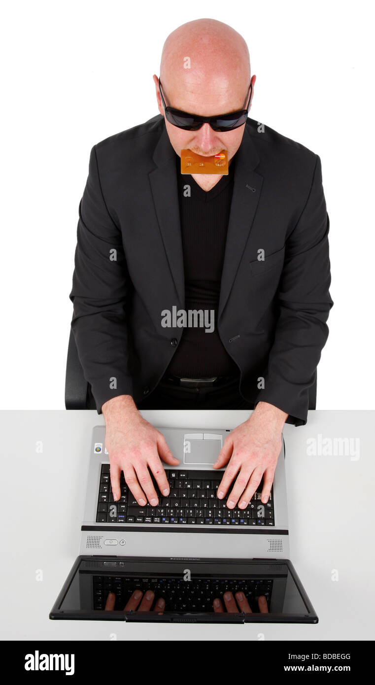 bald headed man with sunglasses and credit card in mouth sitting in front of a laptop Stock Photo