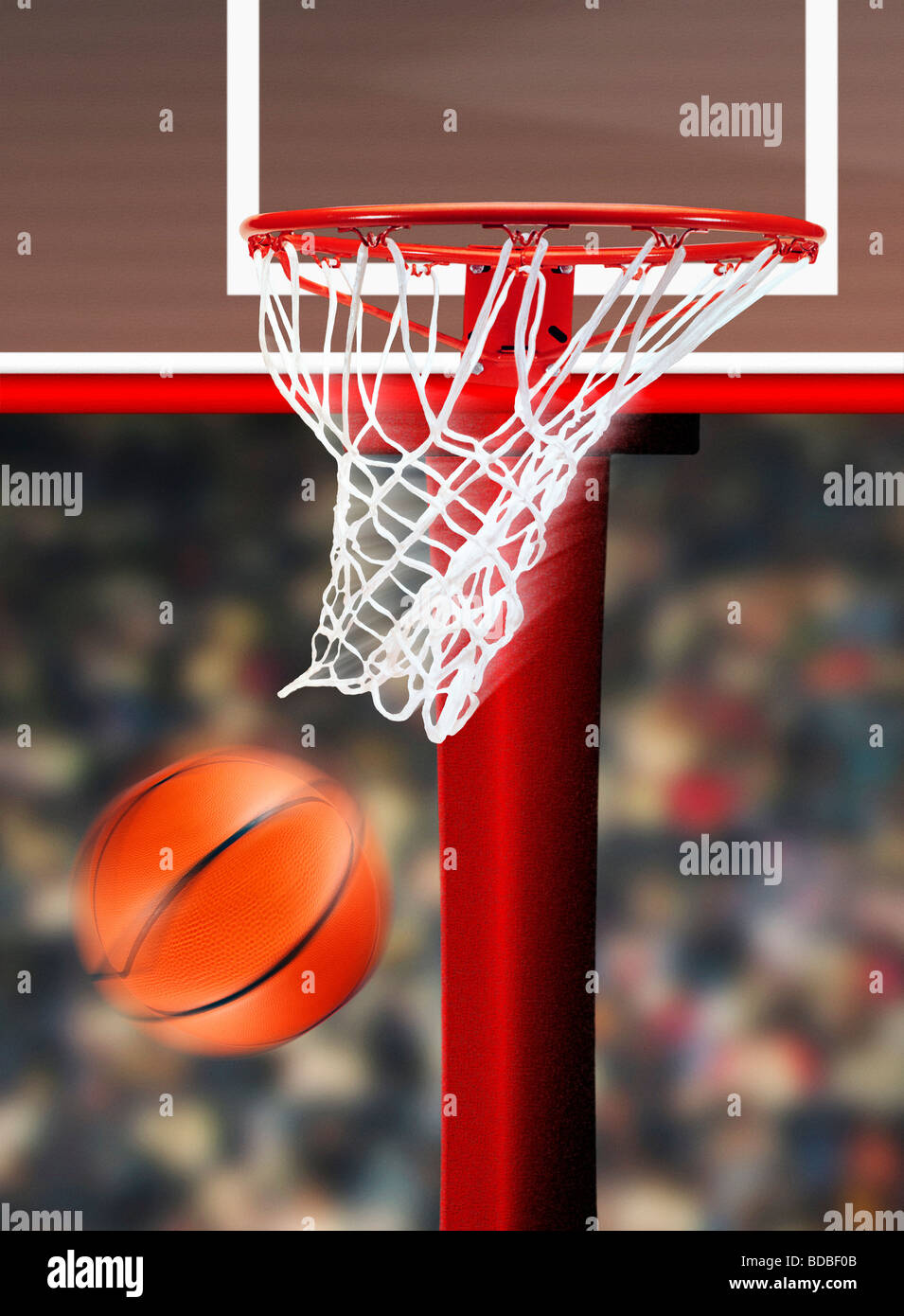 Close up of basketball hoop and pole, with basketball going through hoop and ropes showing movement, sports crowd in background. Stock Photo