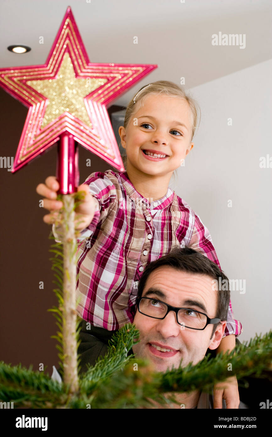 portrait of young girl putting star on top of christmas tree Stock