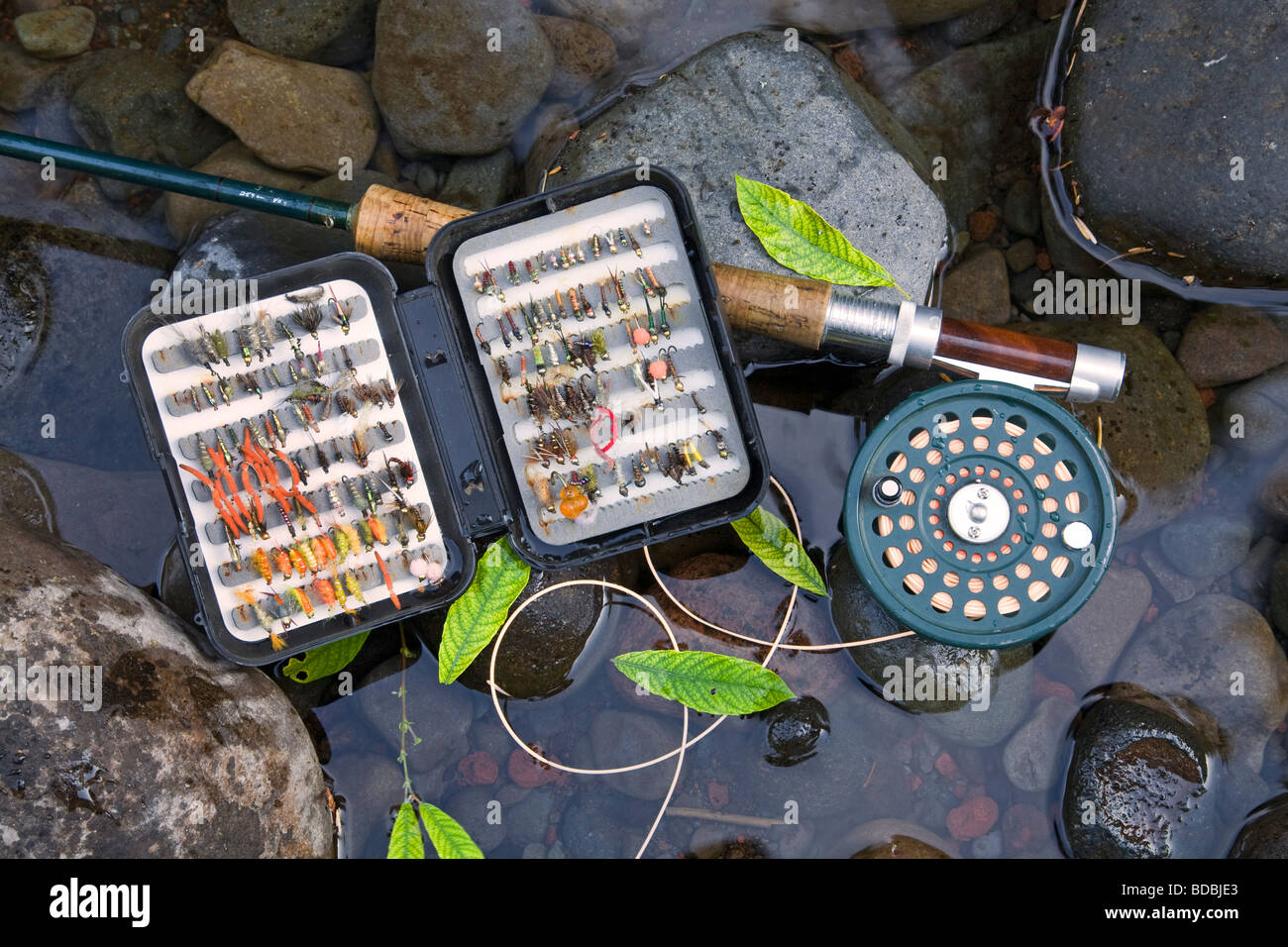 A fly rod, fly reel, trout fishing net, and box of artificial flies used for fly fishing for trout and steelhead Stock Photo