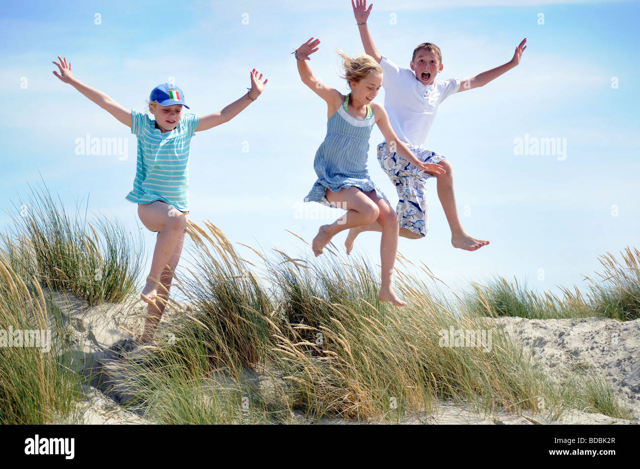 Royalty free photograph of boy and girl jumping off sand dunes on beach