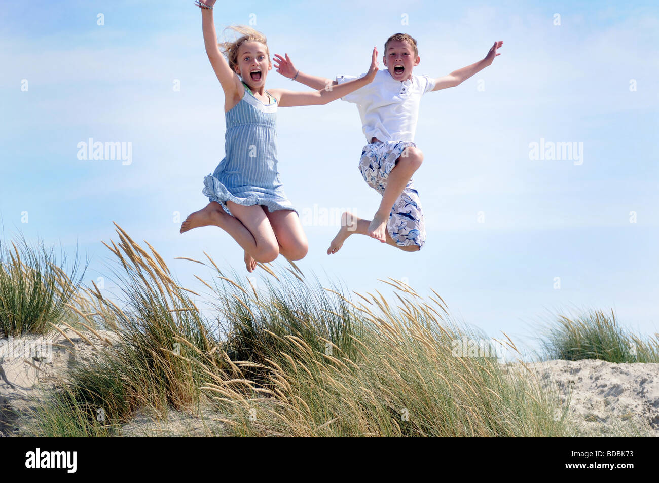 Royalty free photograph of boy and girl jumping off sand dunes on beach