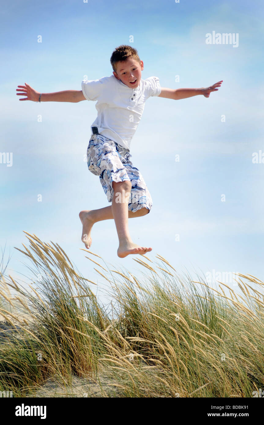 Royalty free photograph of boy jumping off sand dunes on beach in the
