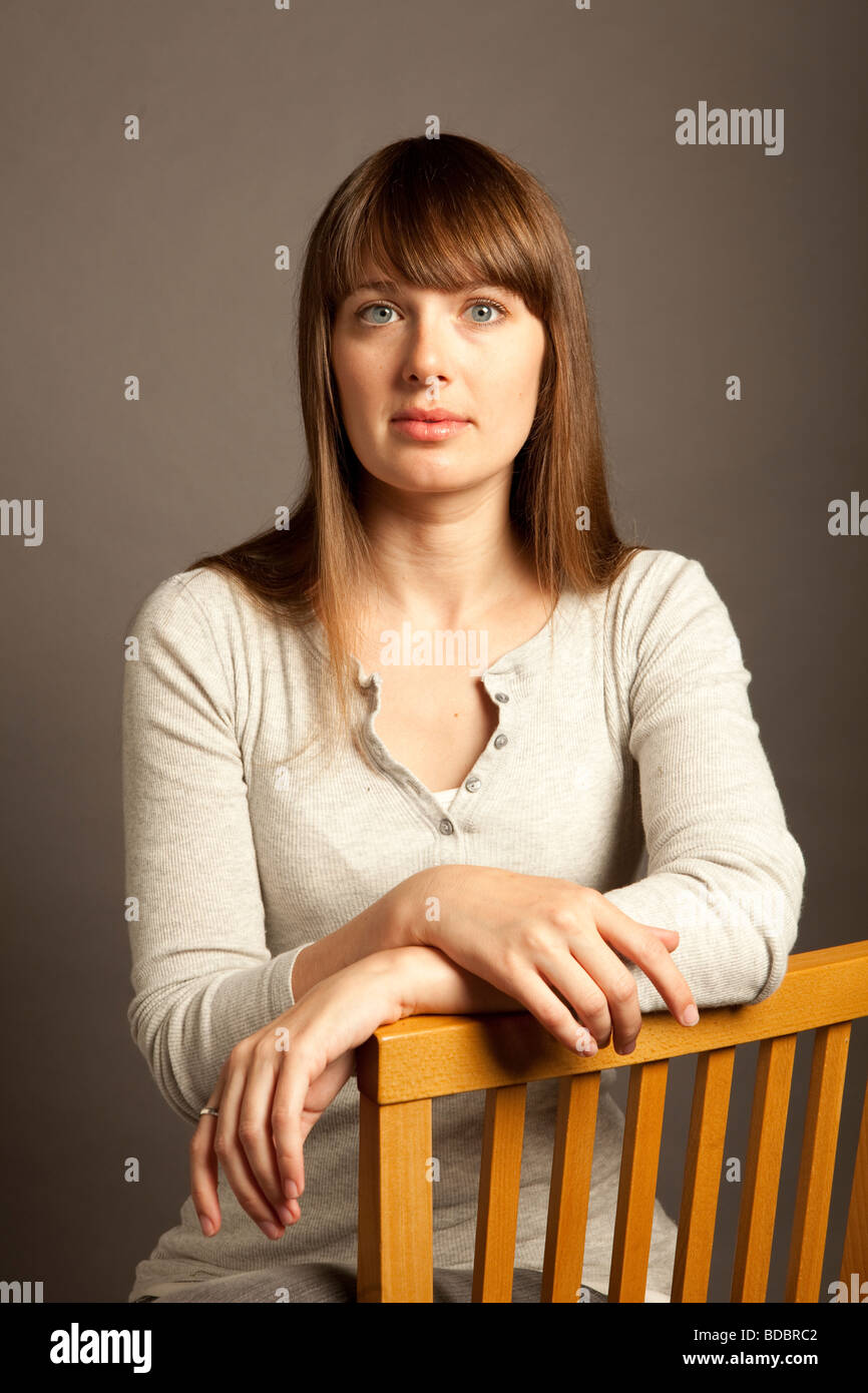 Upper body portrait of a woman with long brown hair and blue eyes sitting in studio. Stock Photo