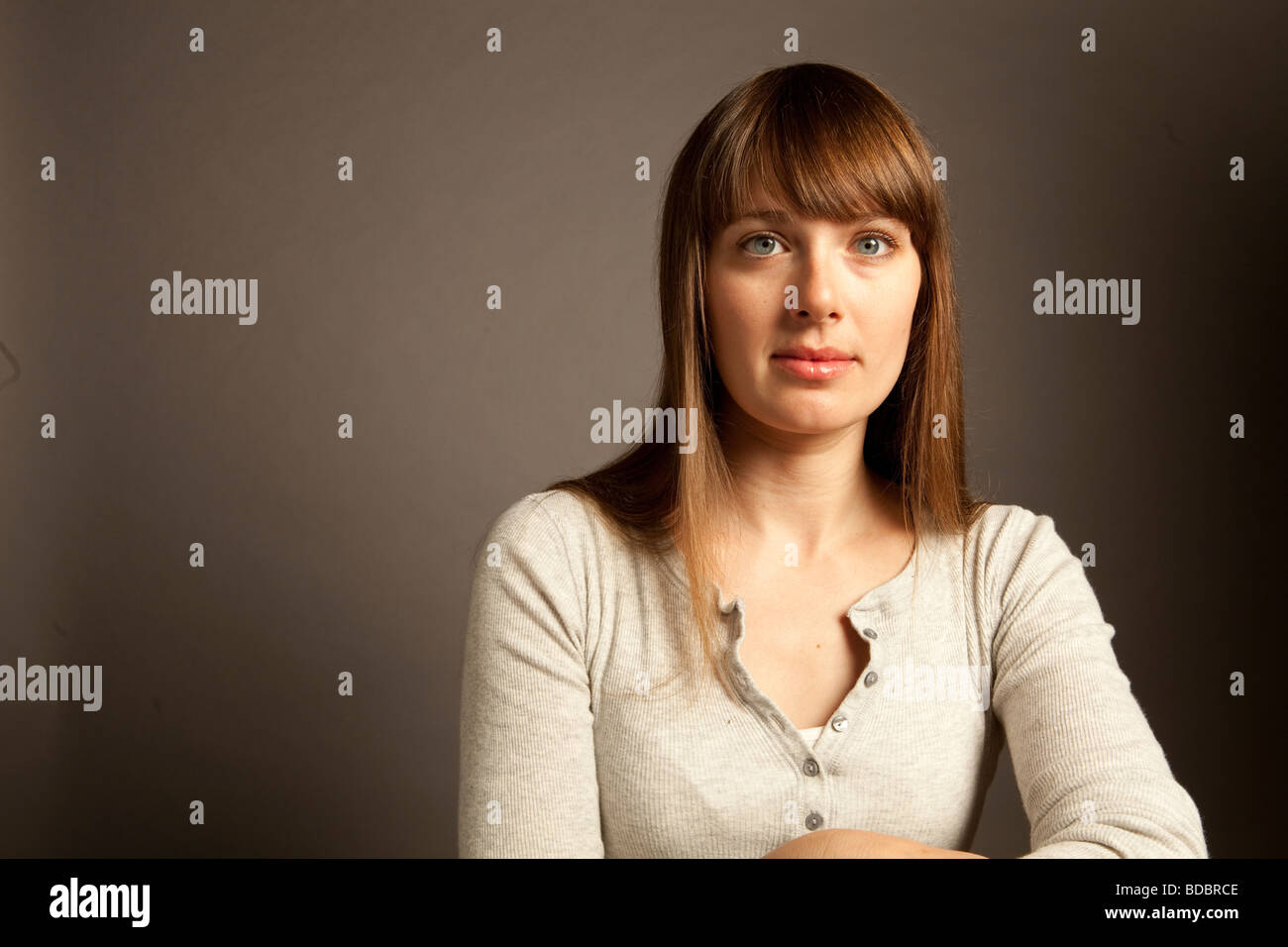 Upper body portrait of a woman with long brown hair and blue eyes sitting in studio. Stock Photo