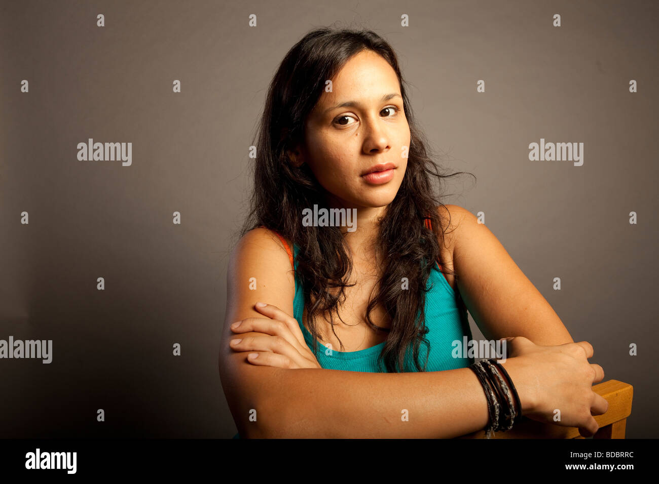 Portrait of Hispanic Latina female against gray background, she has serious expression, looking at camera. Stock Photo