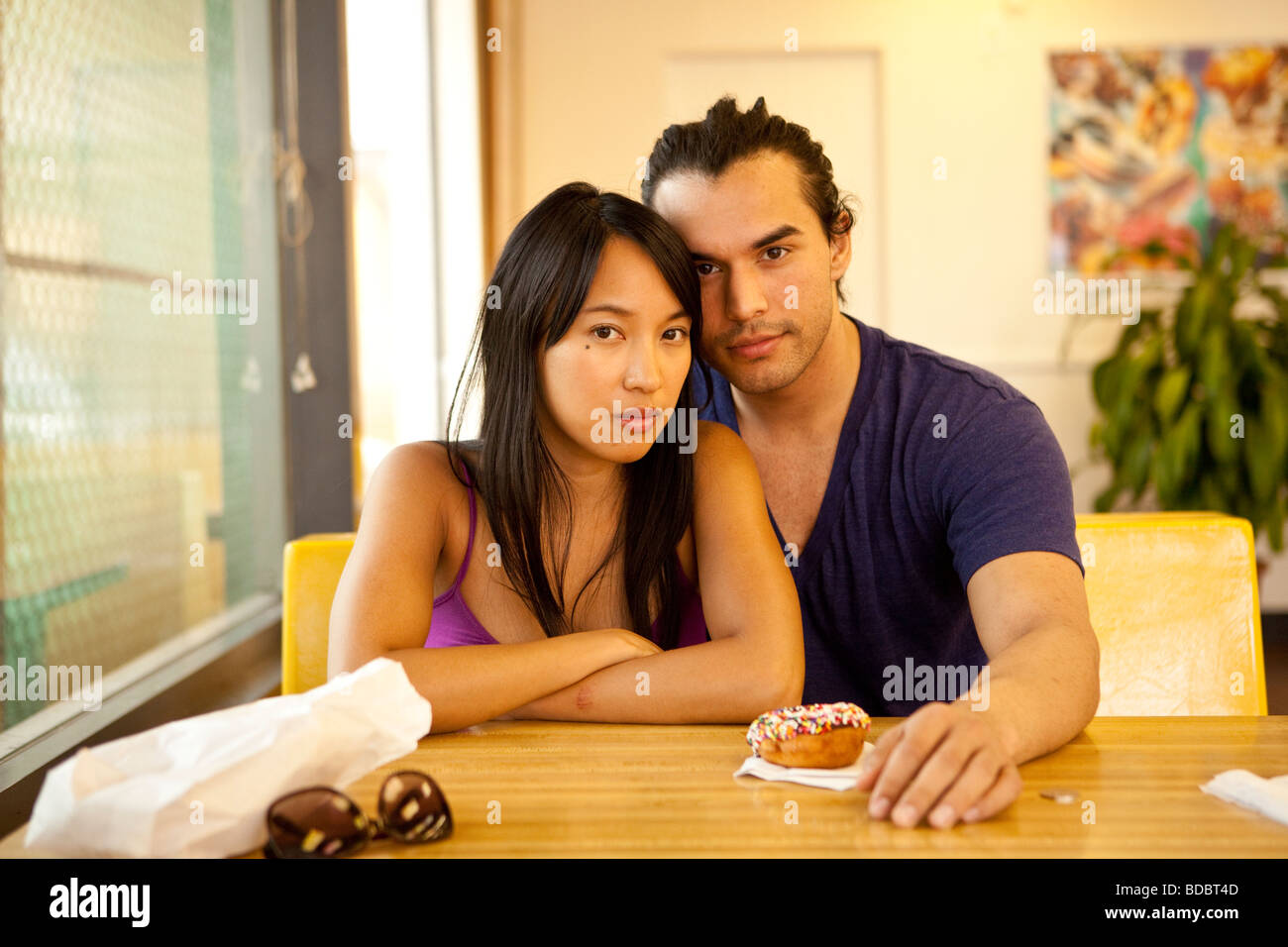 Male Female couple sitting at a table inside a fast food restaurant, looking at camera. Stock Photo