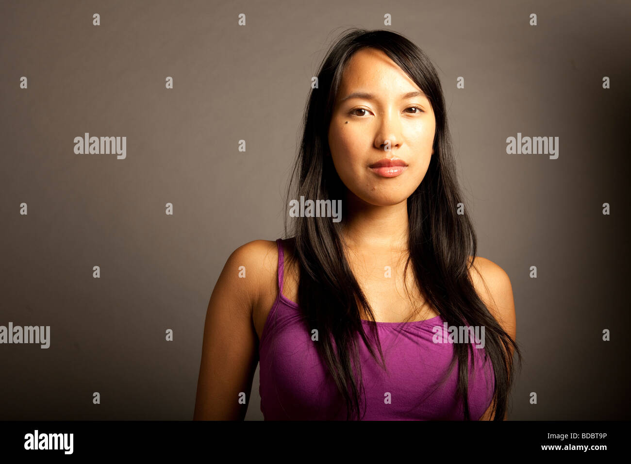 Portrtait of Filipina female wearing purple blouse against gray background, serious expression. Stock Photo