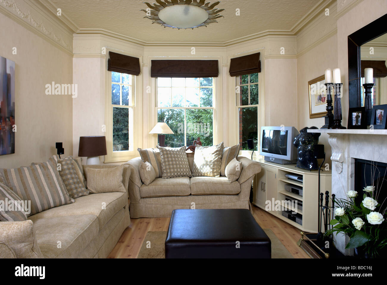 Beige sofas in cream living room with black blinds on bay window and  television on shelf unit beside fireplace Stock Photo - Alamy