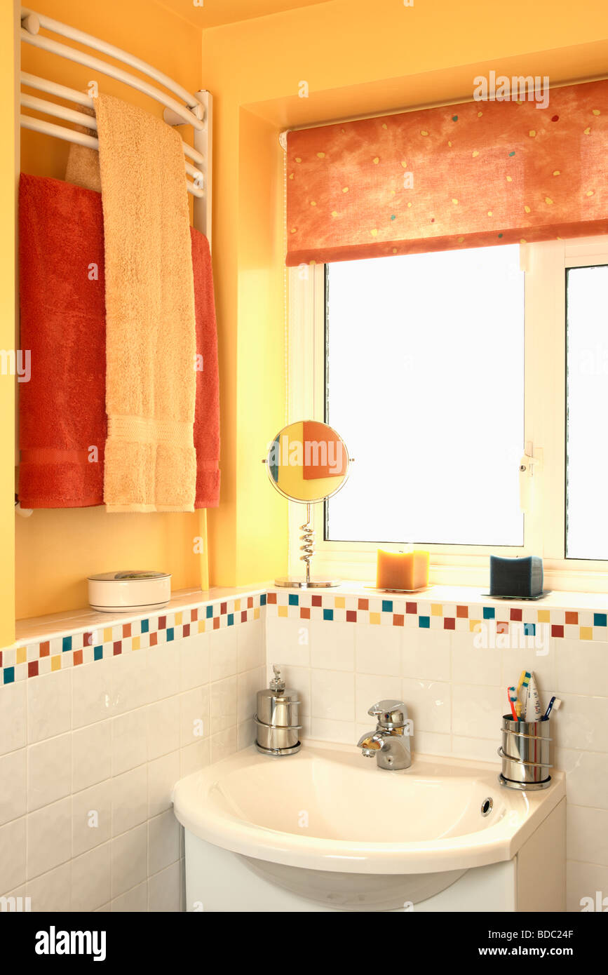 Orange blind on window above white basin in yellow family bathroom with ...