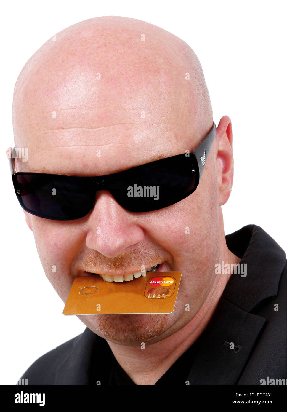 bald headed man with sunglasses and credit card in mouth Stock Photo