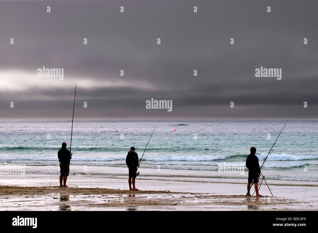 Storm clouds approach as three anglers fish off Sennen beach in Cornwall. Stock Photo