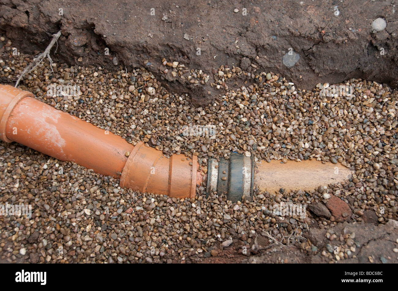 New plastic drain pipe joined to clay pipe in pea gravel Stock Photo
