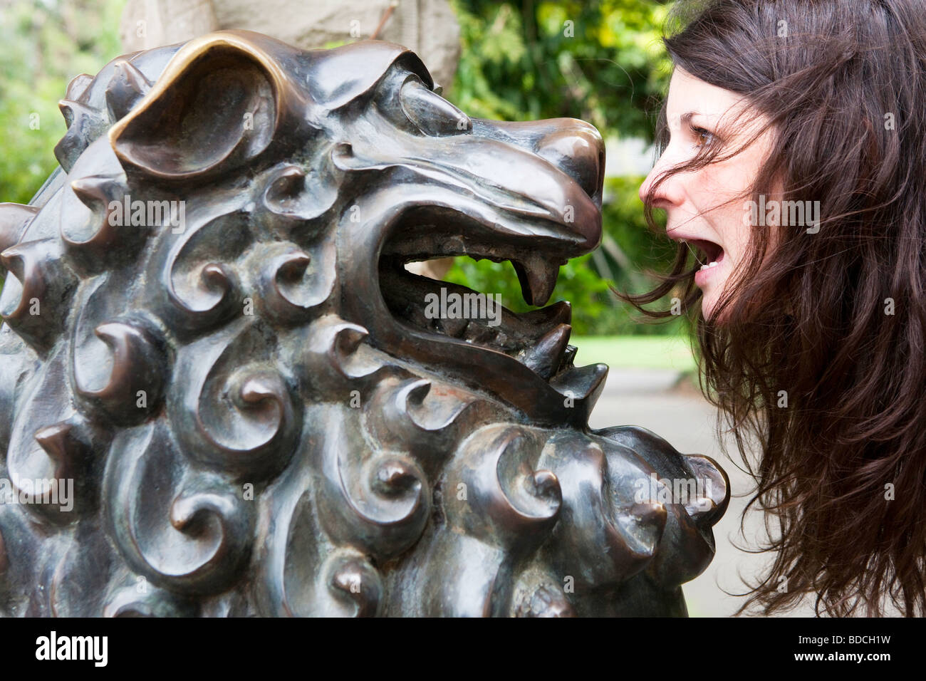 Portrait of a young woman looking at a metal sculpture of a lion in Sydney's Botanic Gardens, Australia Stock Photo