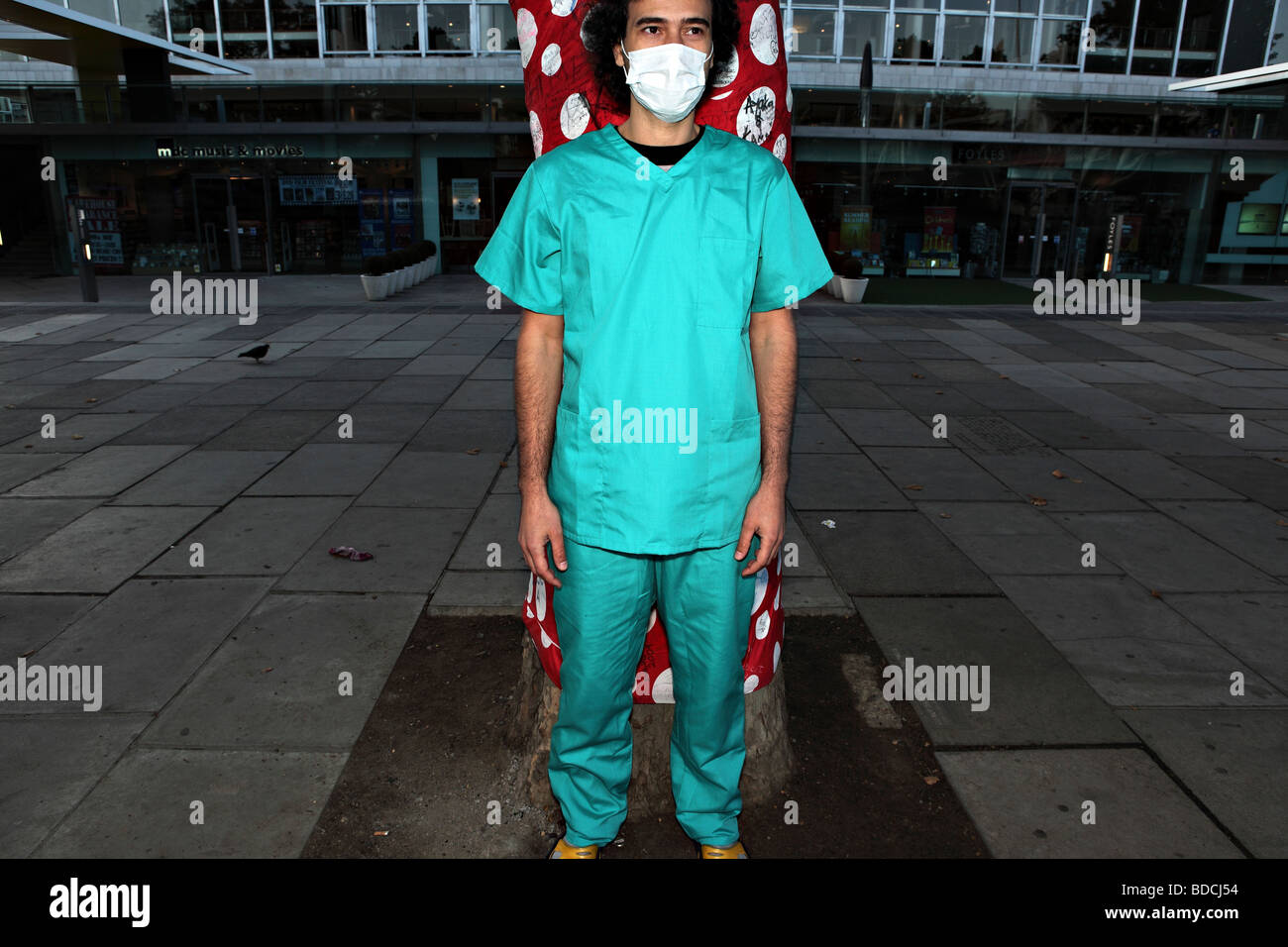 Young man stand sstill on the South Bank, London. He wears a surgical uniform and a face mask. Stock Photo