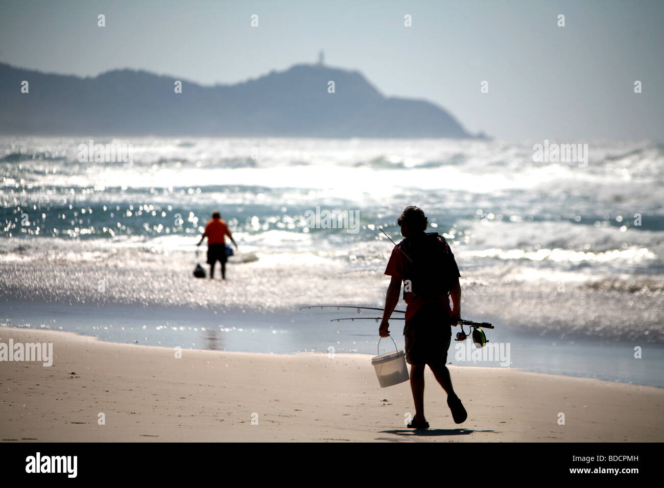 A beach fisherman strolls past a man collecting beach worms at Tallow beach near Byron Bay Australia. Stock Photo
