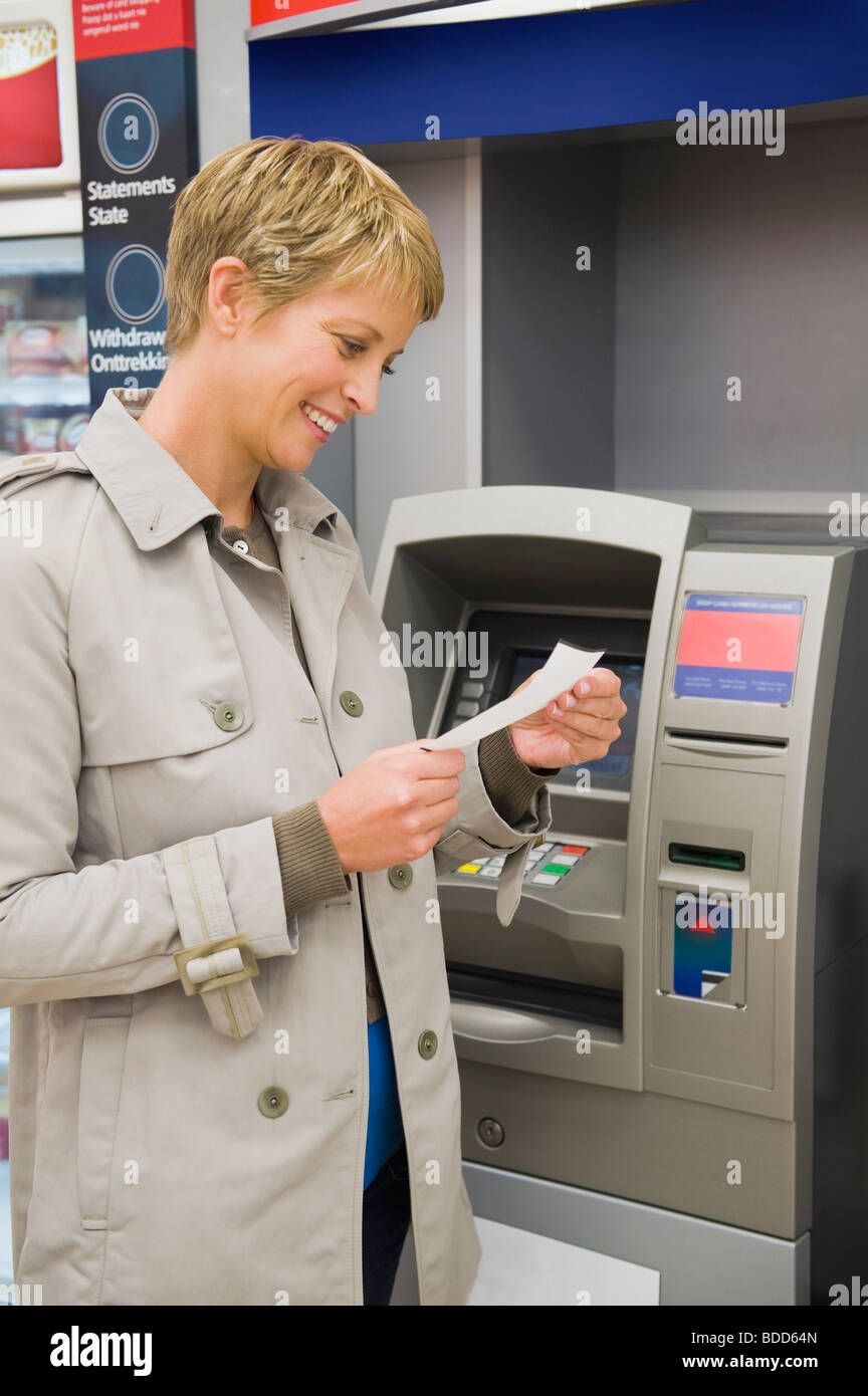 Woman reading a transaction slip at an ATM and smiling Stock Photo