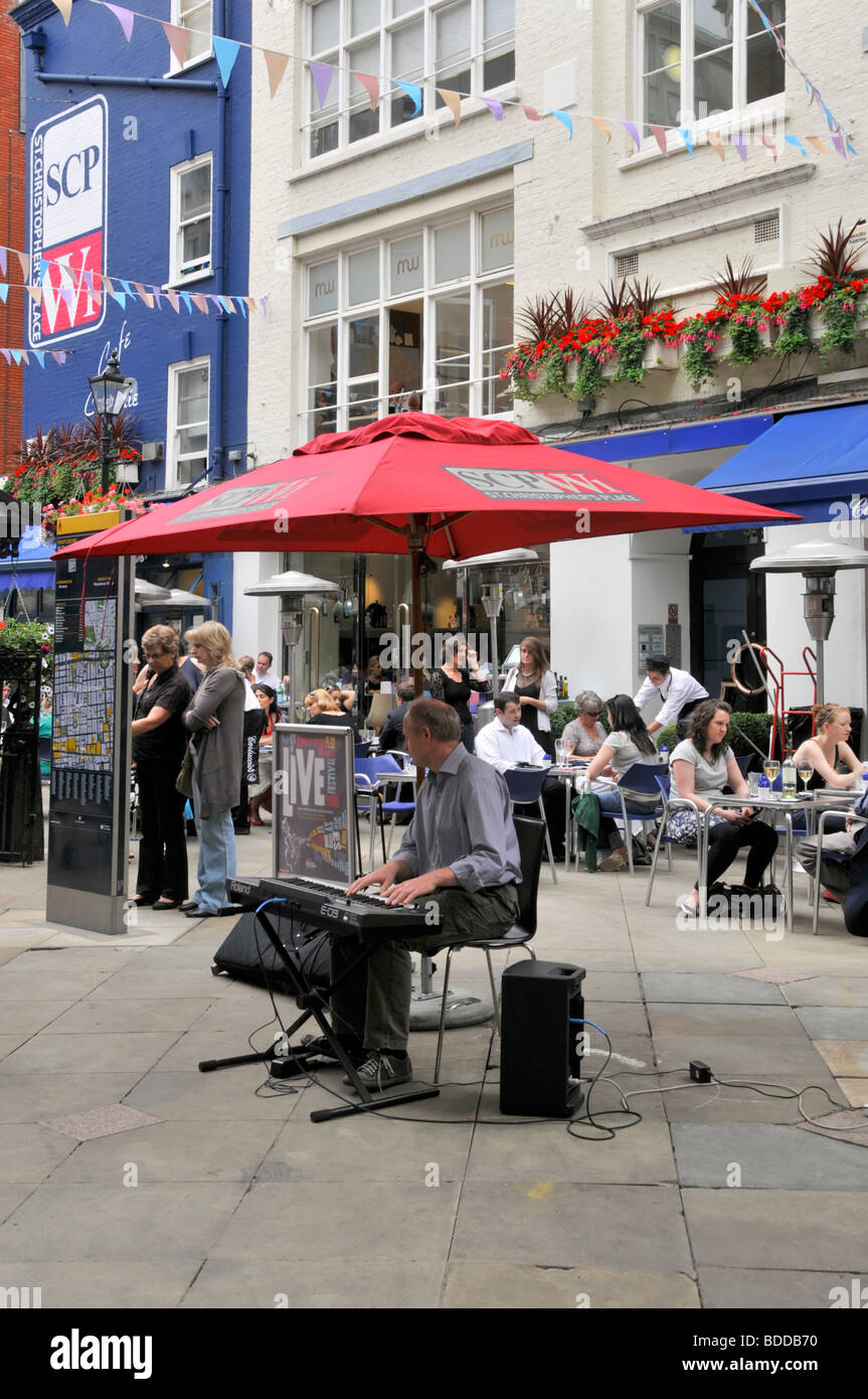 Musician playing outside pavement cafe bars & restaurants in West End