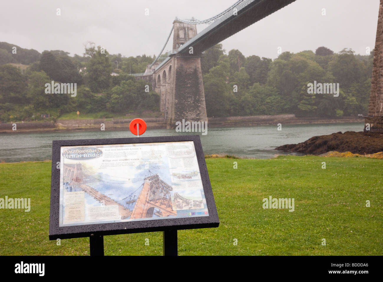 Porthaethwy, Anglesey, North Wales, UK. Menai suspension bridge and information sign by the Menai Strait in pouring rain Stock Photo