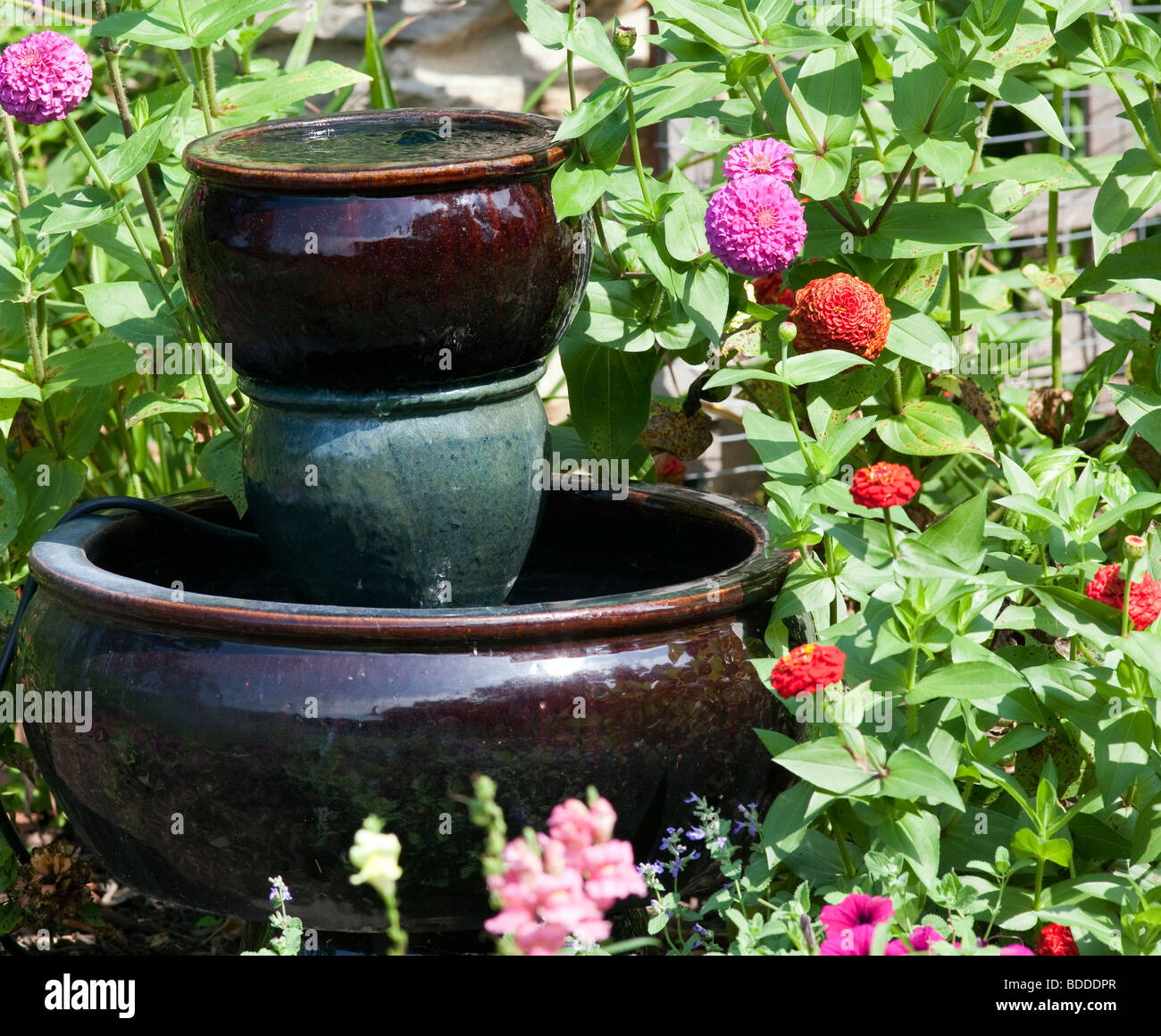 At the corner of the cottage is a fountain surrounded by a bed of Zinnia. Stock Photo