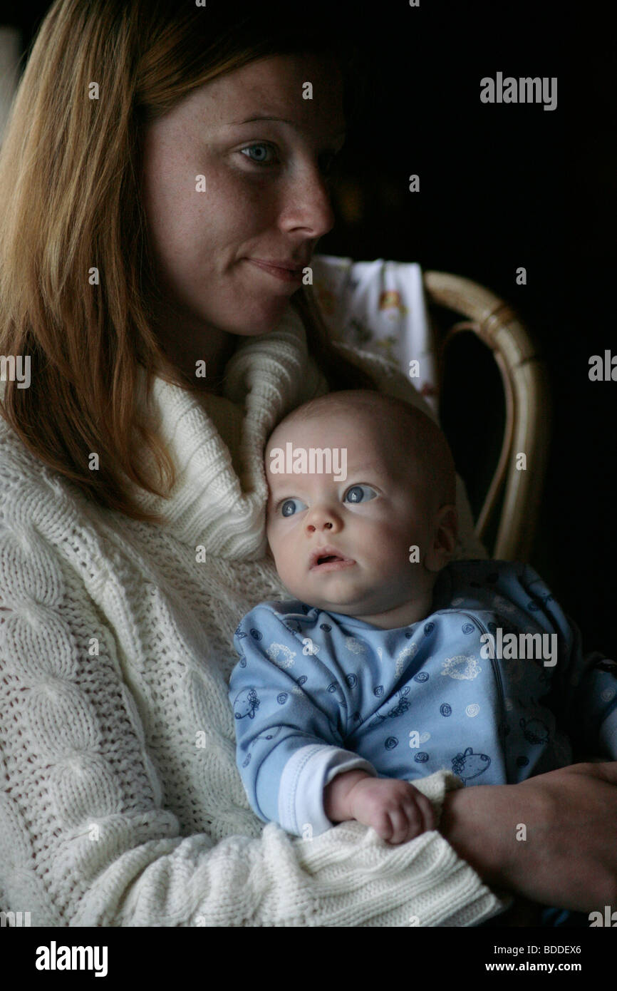 A four month old baby relaxing with his mum in the early morning sat down in a sleep suit. Model released Stock Photo