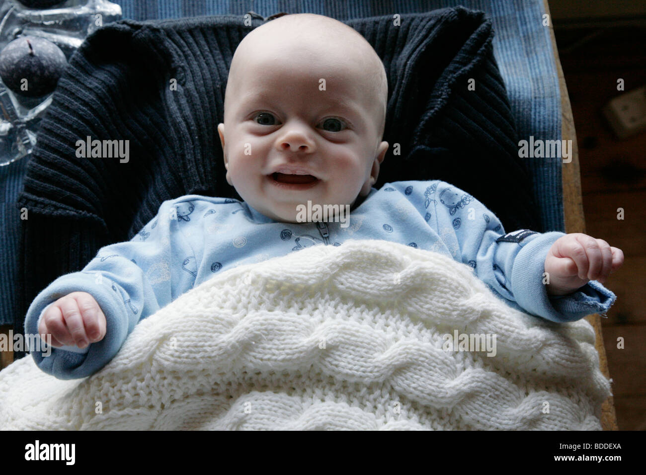 A four month old child being playful in a sleep suit using mum's jumper
