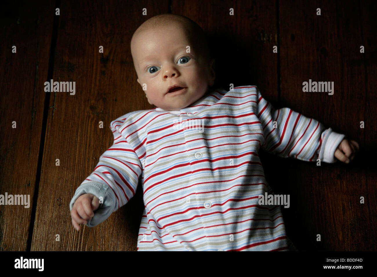 A three month old child being playful in a sleep suit laying on a