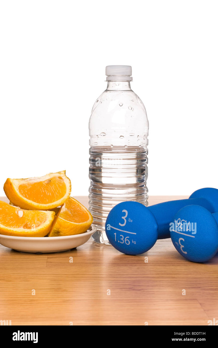 A conceptual image of healthy living including exercise equipment, a bottle of water and a sliced orange. Stock Photo