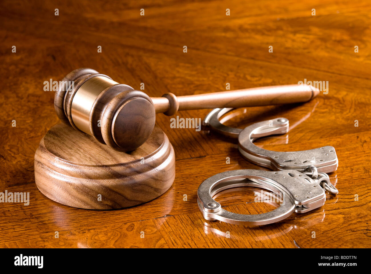 A gavel and block on a richly colored cherry wooden desk with handcuffs. Stock Photo