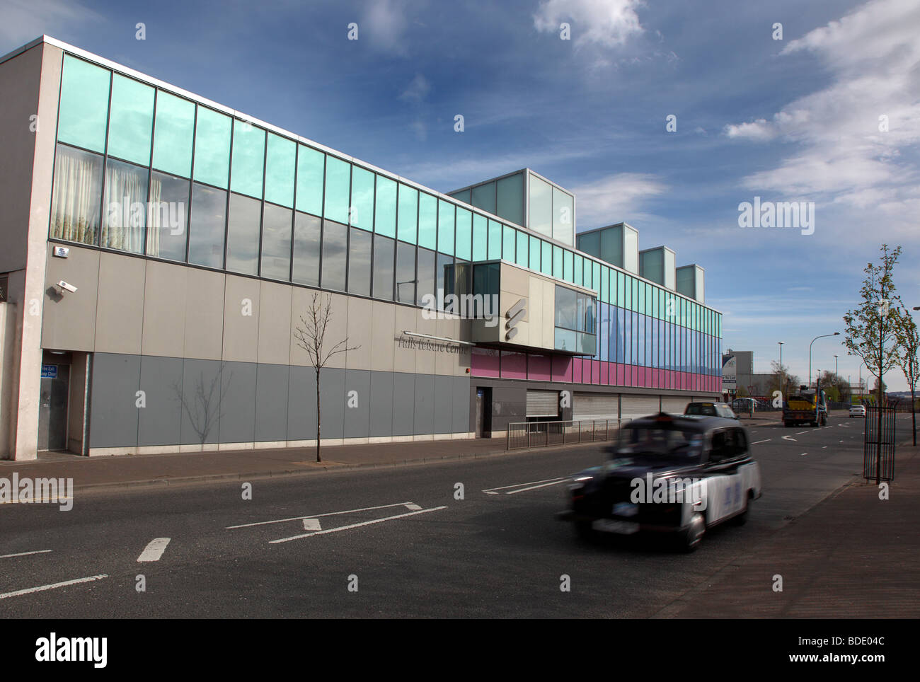 IRELAND, North, Belfast, West, Falls Road, Exterior of the refurbished Falls Swimming Baths with black taxi cab passing by. Stock Photo