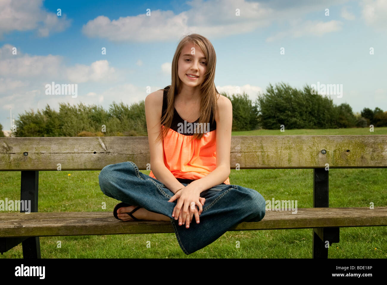 girl sat crossed legged on a bench Stock Photo