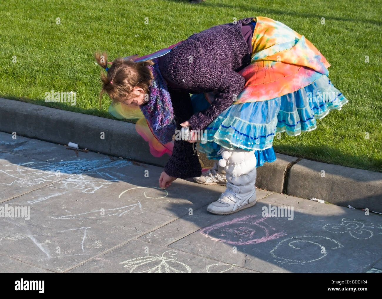 A young woman in colorful clothing draws designs on the street with chalk during Olympia's annual Arts Walk. Stock Photo