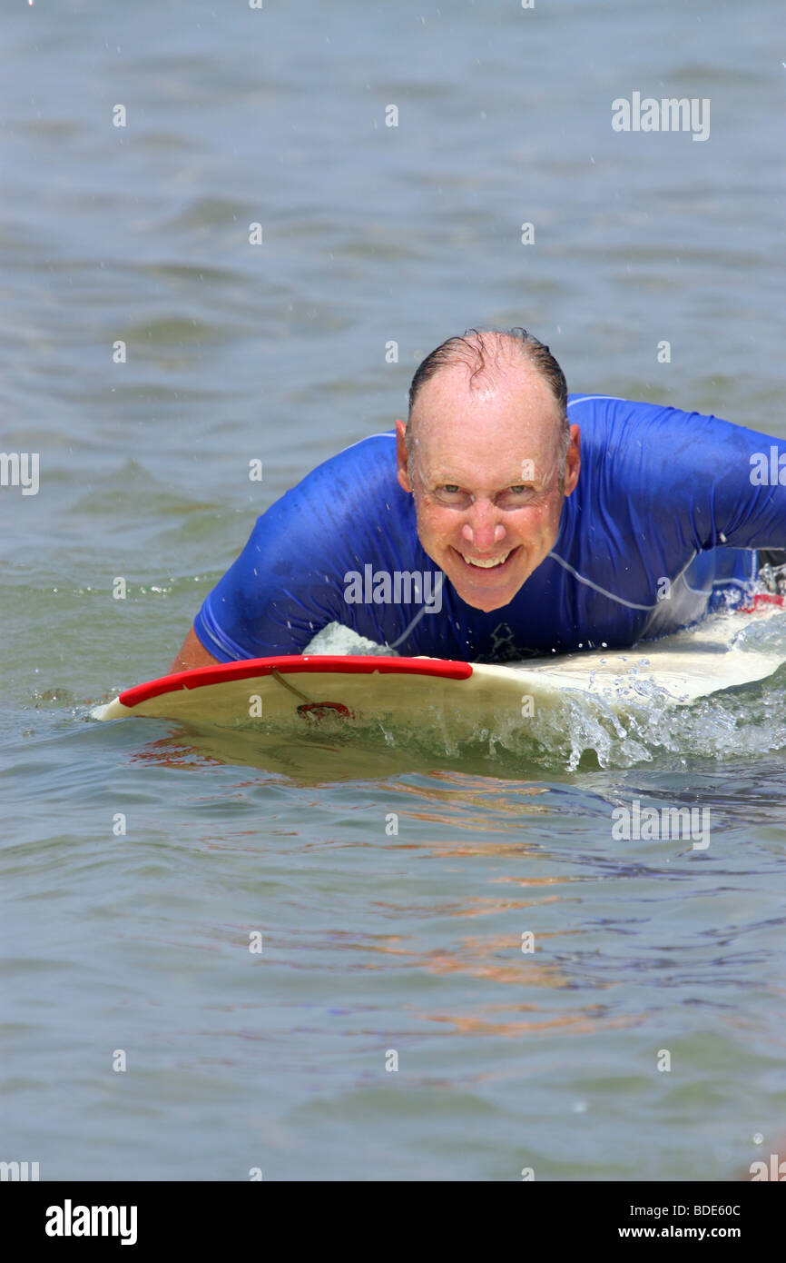 Older man paddling surfboard Stock Photo