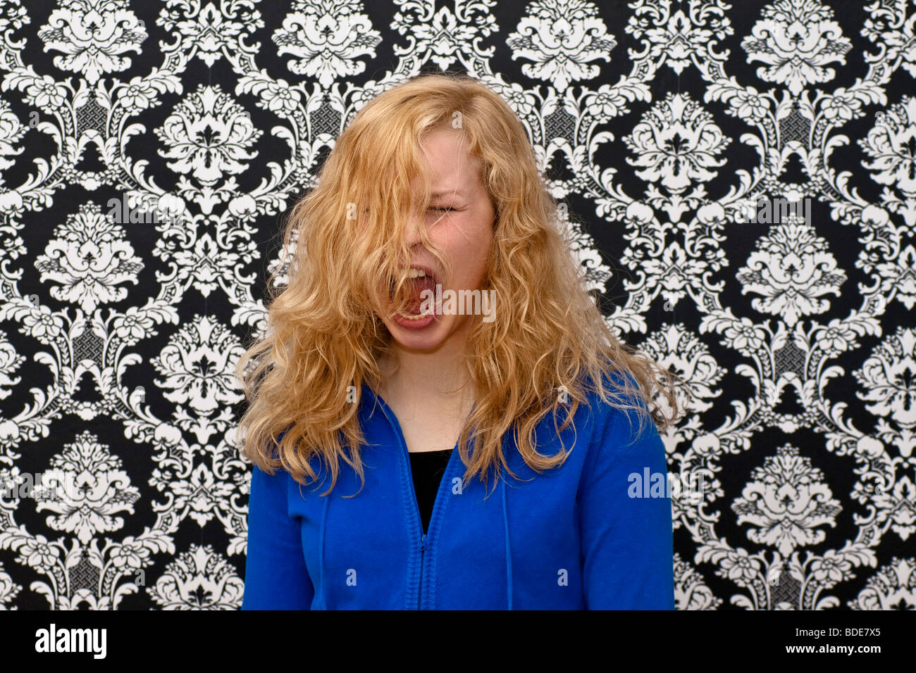 bond girl with a blue sweat shirt in front of a black & white figured wallpaper Stock Photo