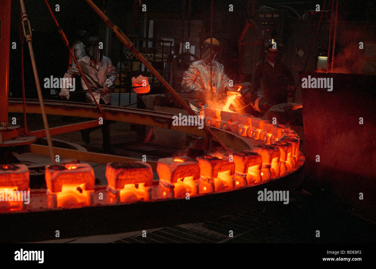 A worker pours molten steel into red hot ingot molds at a foundry in