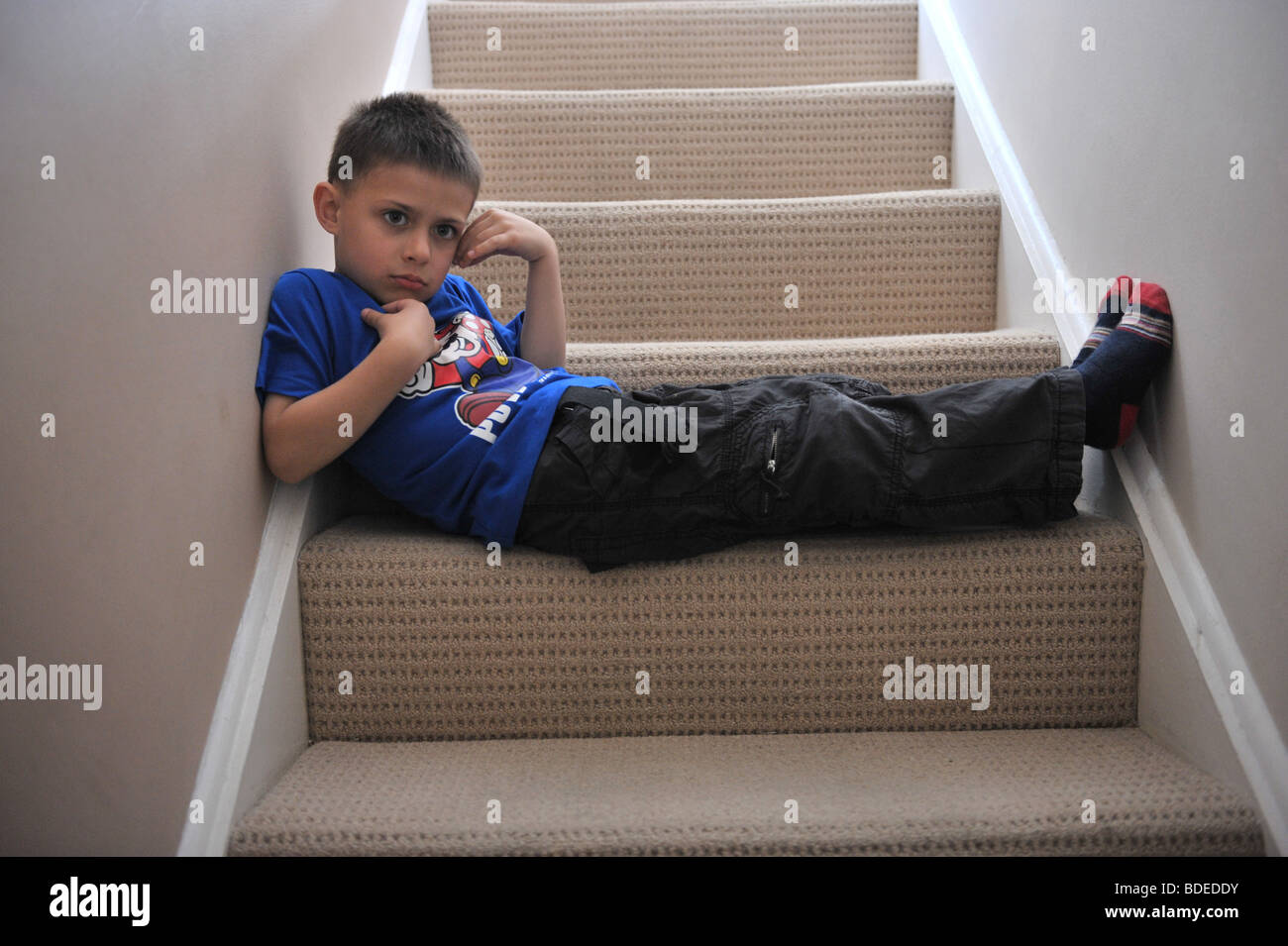 A six year old boy sits on the stair case of his home after being told off. Stock Photo