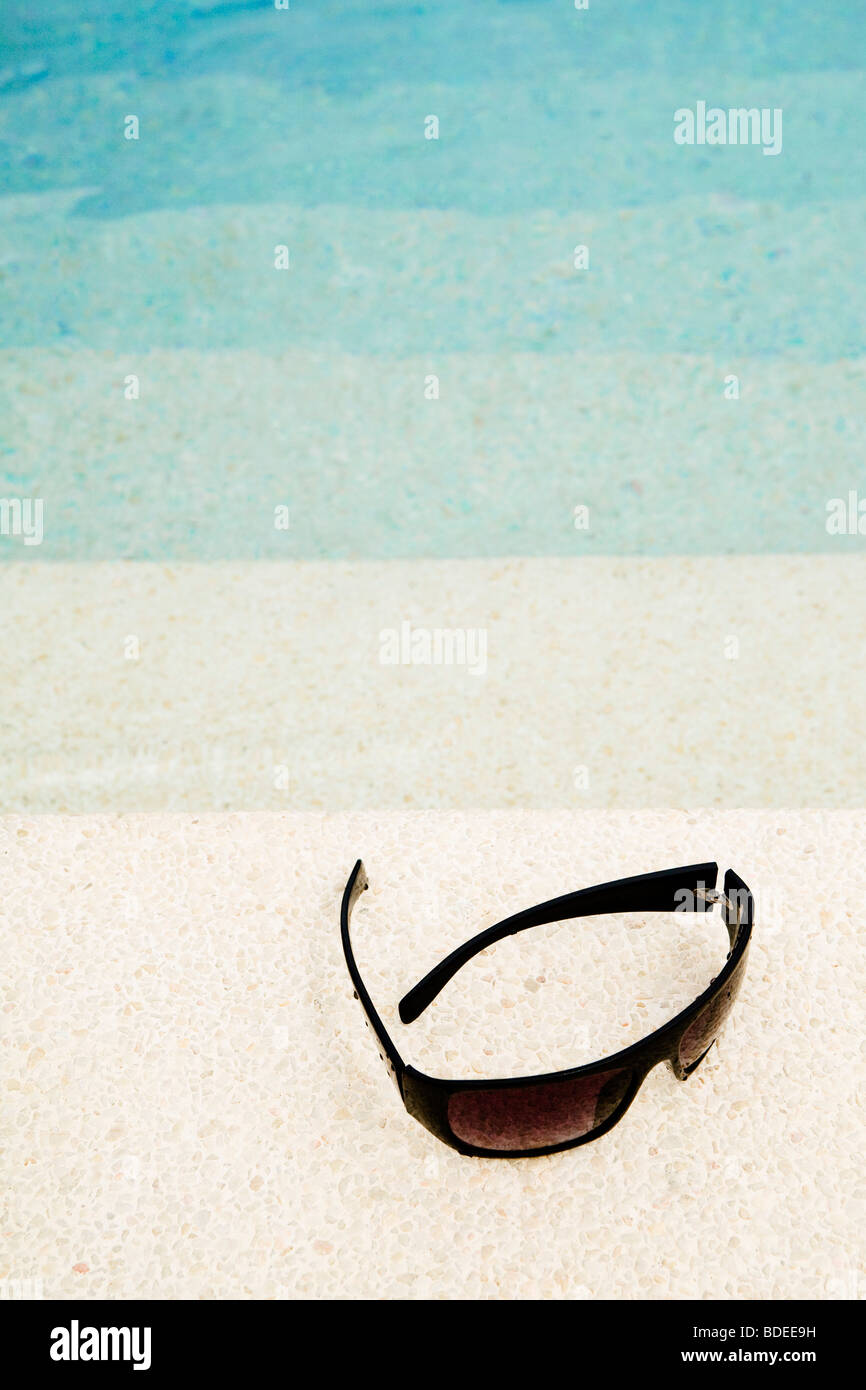 A pair of sunglasses on the edge of a swimming pool Stock Photo