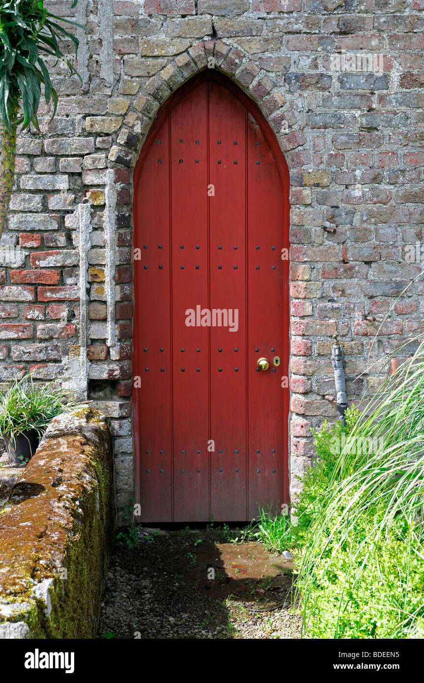 path leading to a narrow red wooden door of a rustic old cottage Stock Photo