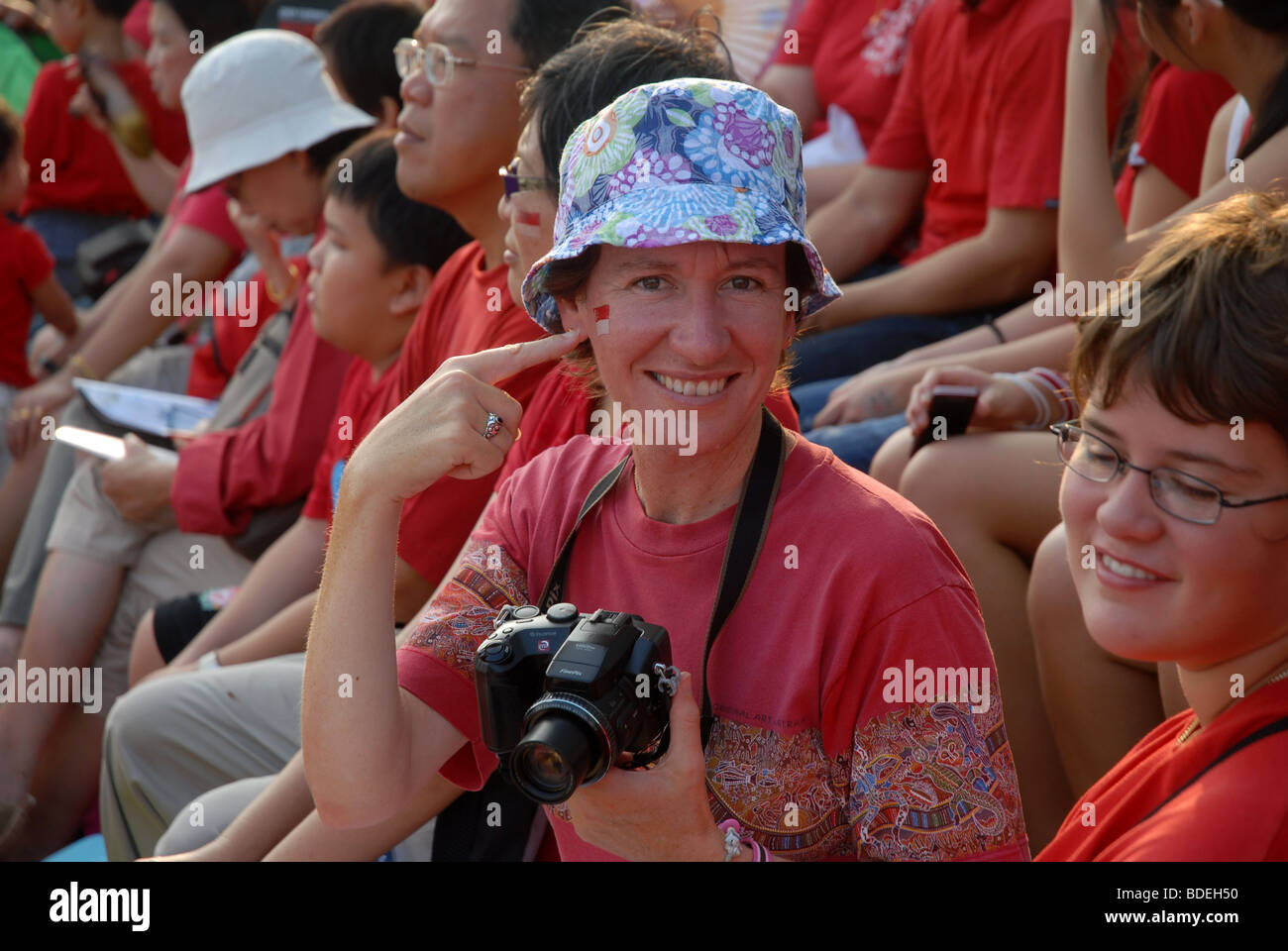 woman pointing at Singapore tattoo on her face, and spectators at National Day Parade Celebrations, 9th August 2009, Singapore Stock Photo