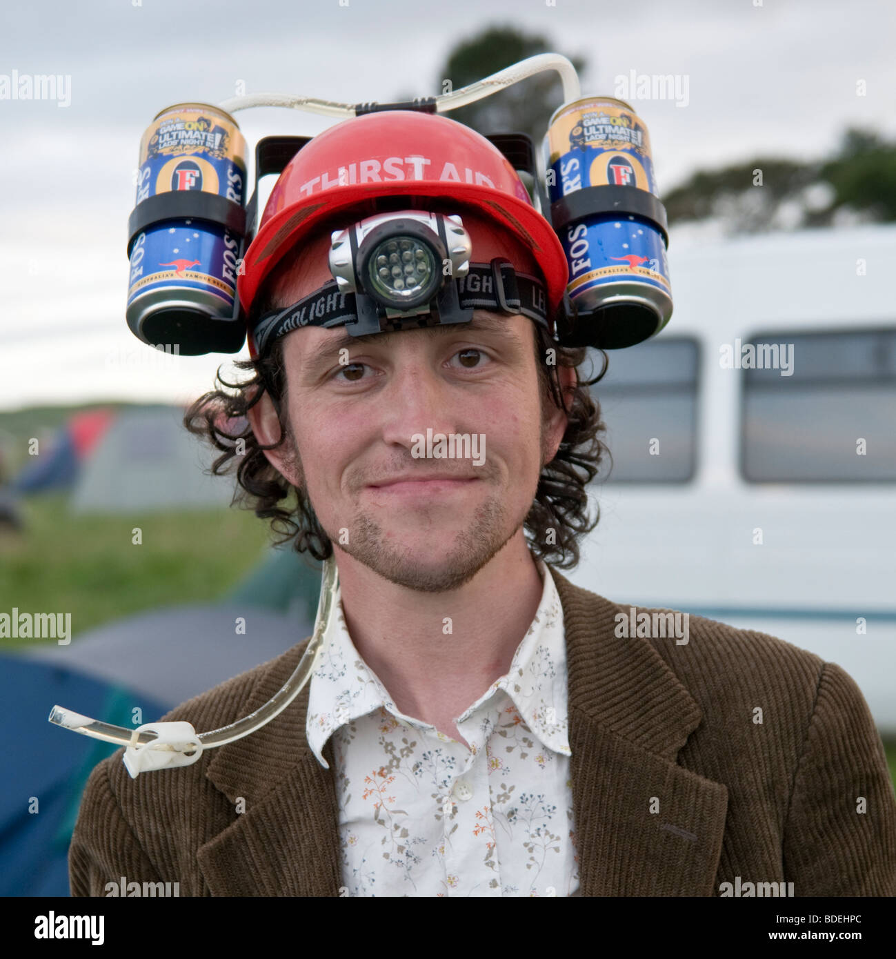 A man with two cans of Fosters beer lager strapped to a helmet on his head at The Square Music Festival, Borth, July 2009. Stock Photo