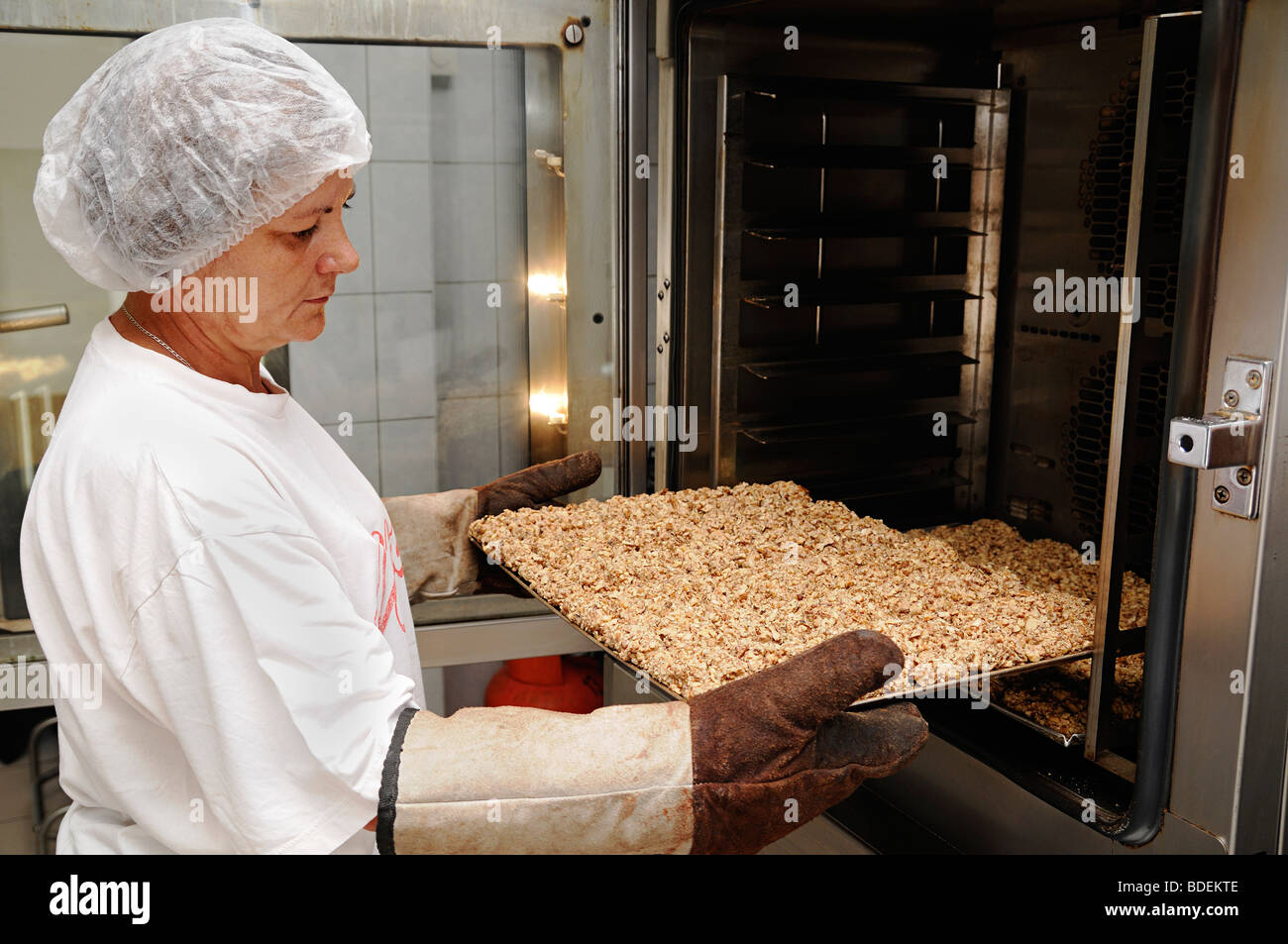 Woman Removing a Tray or Cookies from an Oven in a Commercial Bakery Stock Photo