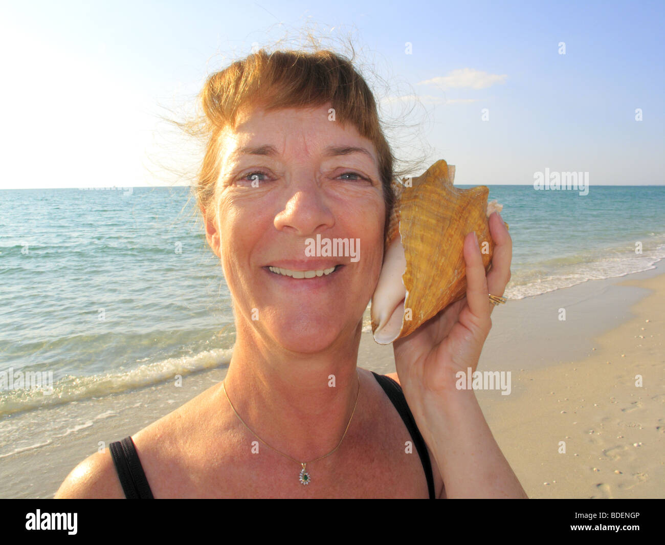 woman listening to sea sounds in a queen conch shell Stock Photo