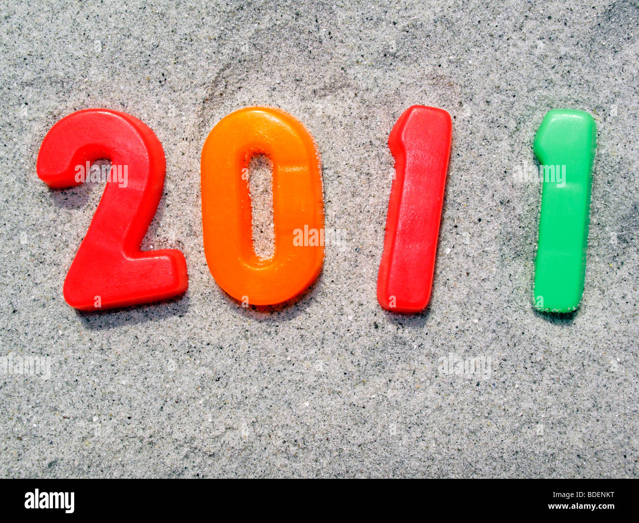Year 2011 in red orange and green numbers on a background of sand Stock Photo