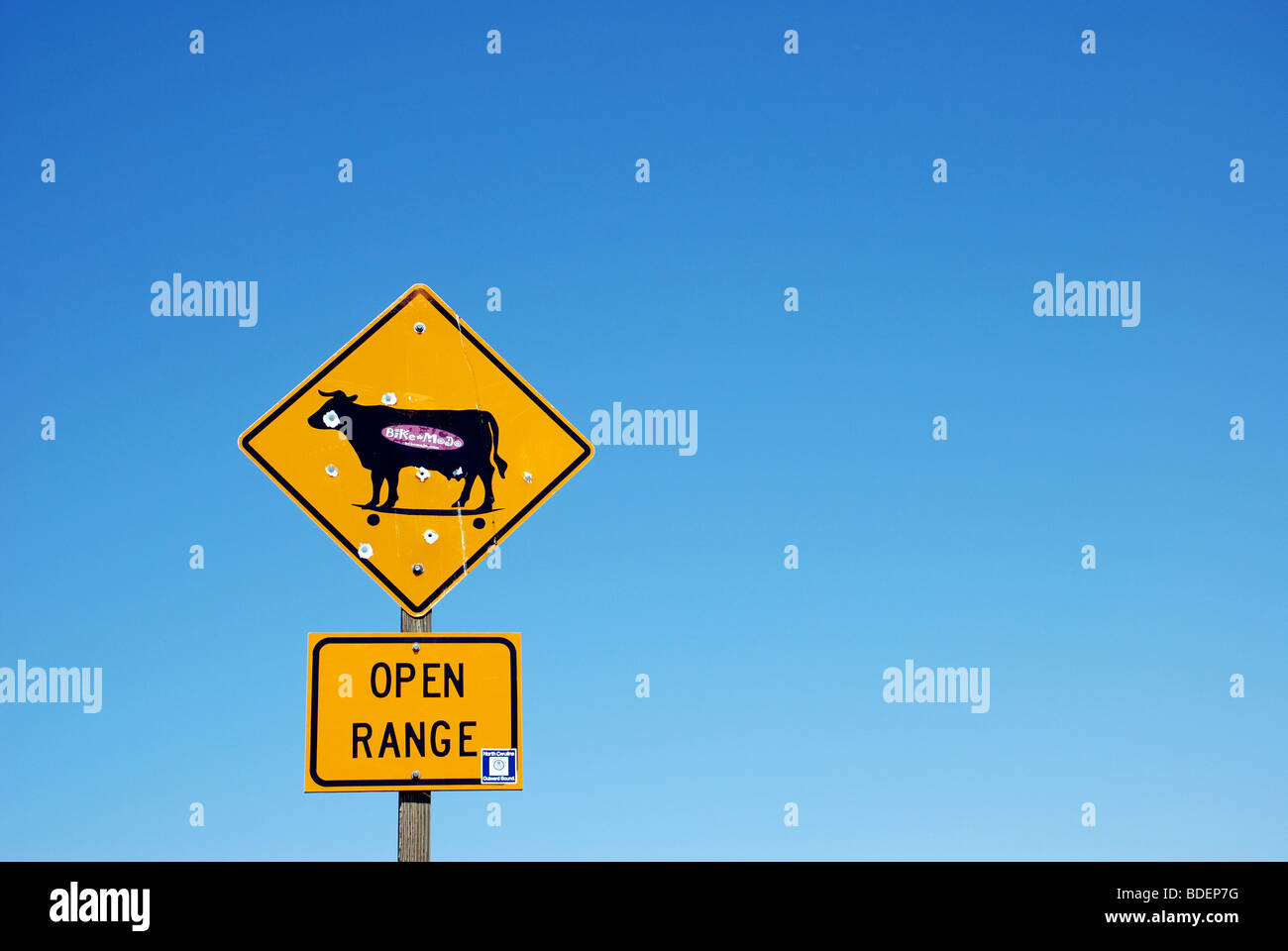 Yellow "Open Range" traffic sign with bullet holes against clear blue sky. Stock Photo