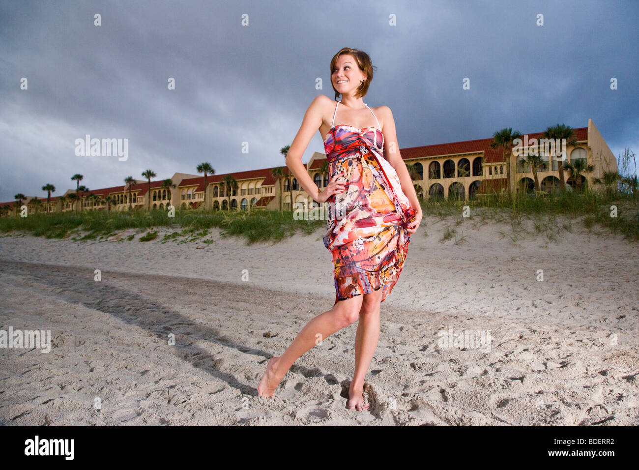 Young woman in colorful sundress standing on beach in front of resort ...