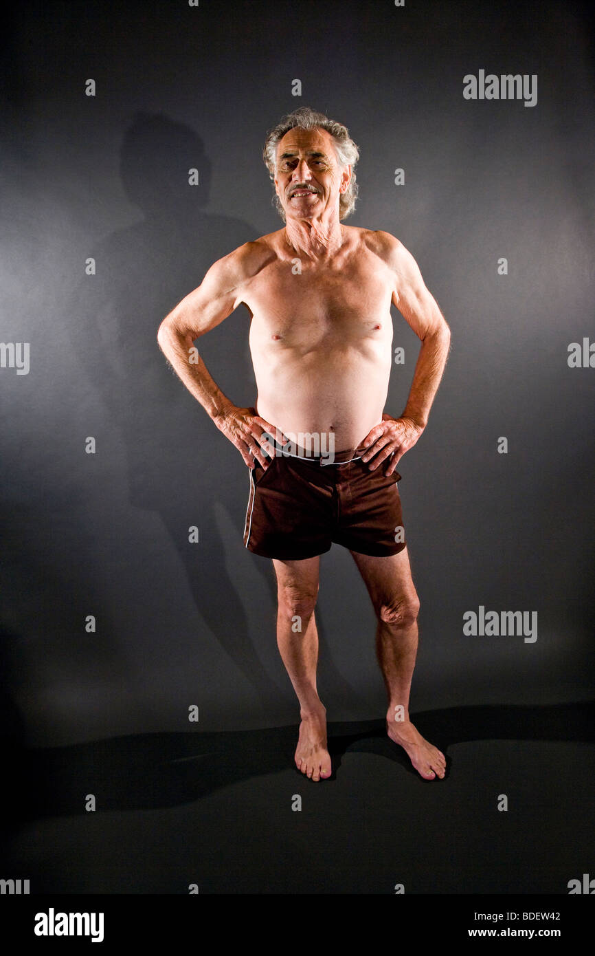 Happy senior man in boxer shorts standing against gray background