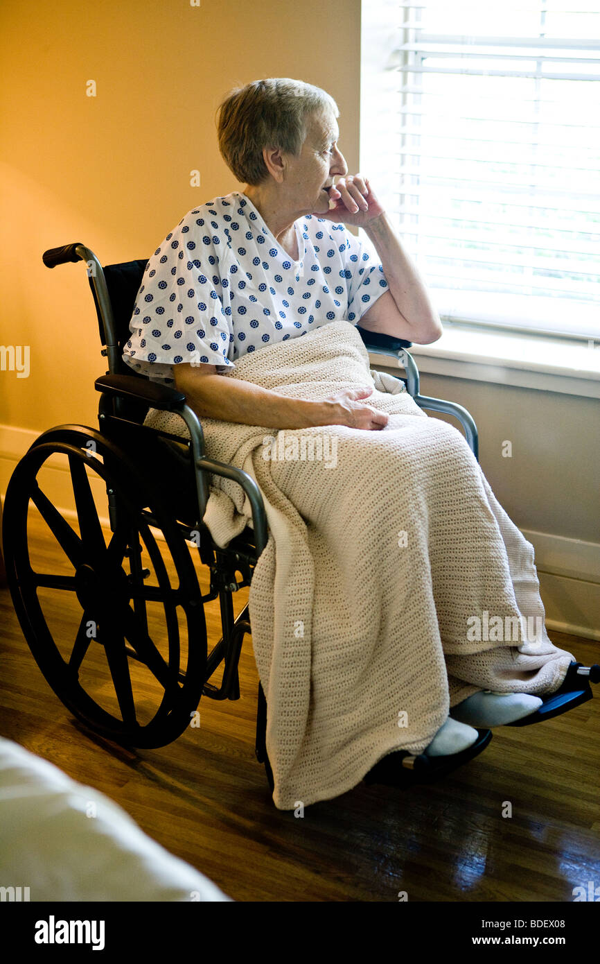 Pensive elderly woman in wheelchair looking out window Stock Photo