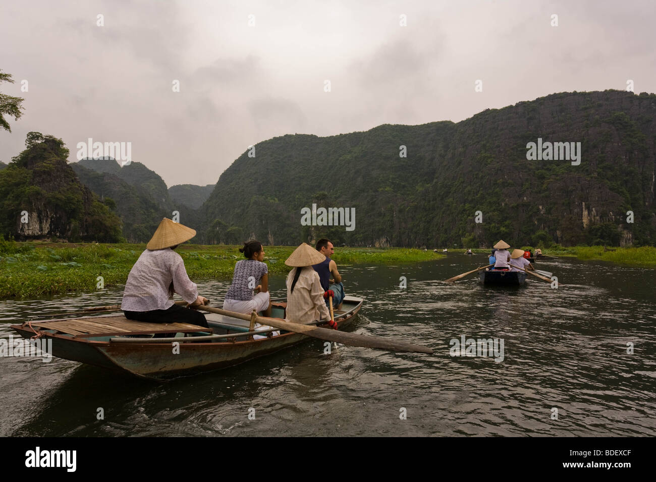 Local women steer small boats along waterways between massive limestone cliffs, Hoa Binh, Vietnam Stock Photo